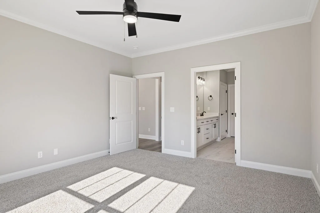 Bright, spacious bedroom with beige walls, carpet, ceiling fan, and attached bathroom by Pratt Home Builders in Chattanooga TN.
