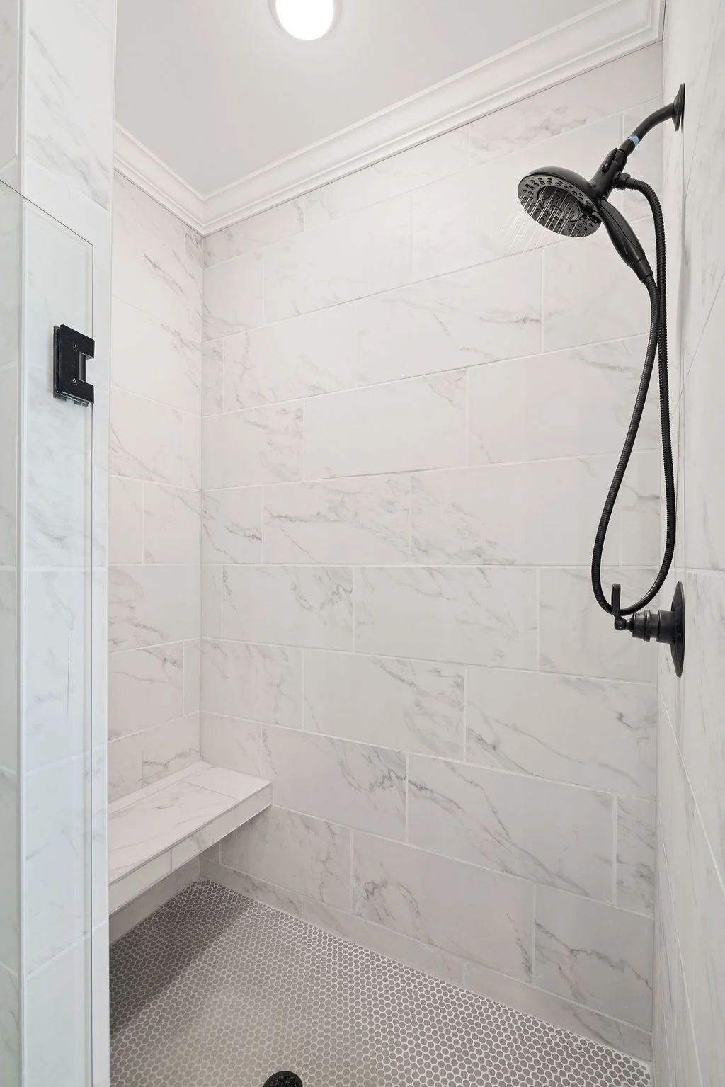 Modern shower by Pratt Home Builders in Chattanooga TN, featuring white marble tiles, a built-in bench, and a black showerhead.