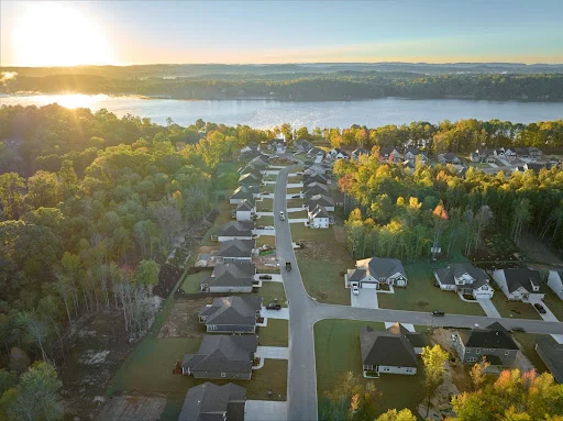 Aerial view of a suburban neighborhood near a river at sunrise, featuring Pratt Home Builders in Chattanooga TN, surrounded by lush trees.