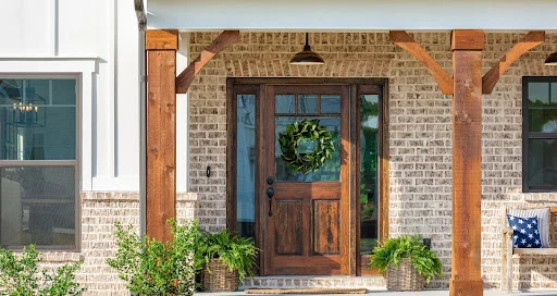 Charming porch with rustic wooden door and columns, decorated with a wreath and plants. Built by Pratt Home Builders in Chattanooga TN.