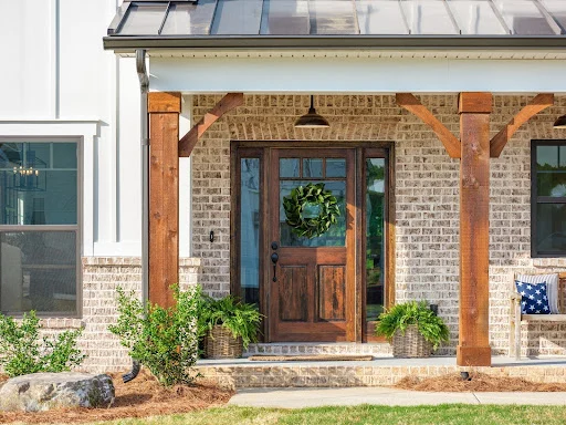Charming porch with rustic wooden door and columns, decorated with a wreath and plants. Built by Pratt Home Builders in Chattanooga TN.