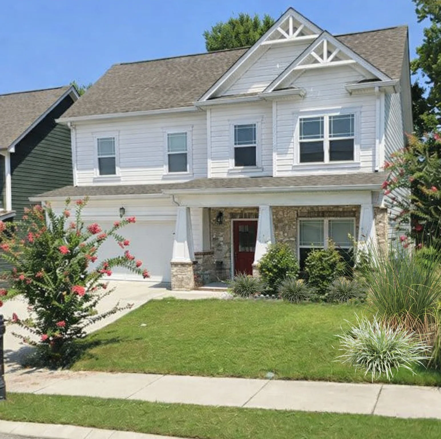 Two-story white house with stone accents and a front porch. Landscaping includes shrubs and flowering trees. Built by Pratt Home Builders in Chattanoo