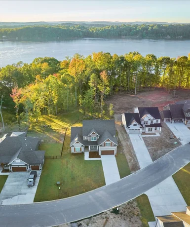 Aerial view of modern homes by a lake, surrounded by trees, built by Pratt Home Builders in Chattanooga TN, showcasing scenic neighborhood layout.