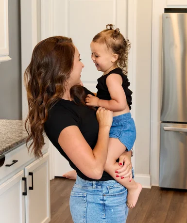Woman holding a smiling toddler in a modern kitchen, showcasing Pratt Home Builders in Chattanooga TN.