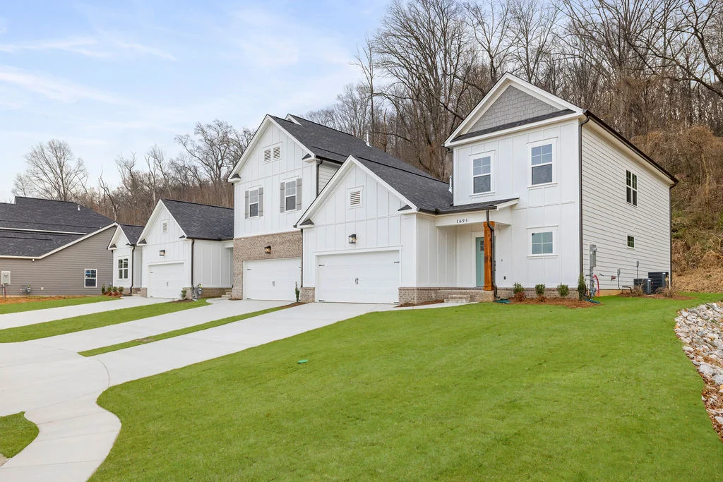 New Home Chattanooga TN. Row of modern, white houses with garages on a grassy slope by Pratt Home Builders. Woods in the background.