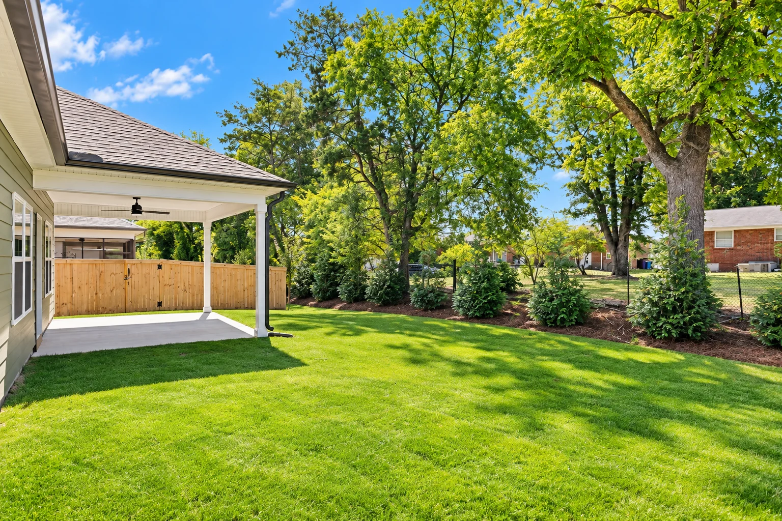 Backyard with lush grass, covered patio, wooden fence, and trees, showcasing Pratt Home Builders’ design in Chattanooga, TN.