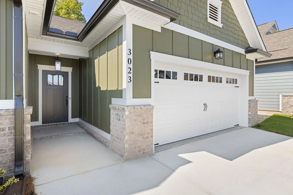 Modern green and white house exterior by Pratt Home Builders in Chattanooga TN, featuring a dark front door and a white garage.