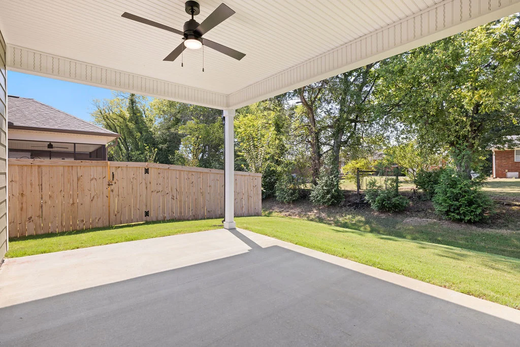 Covered patio with ceiling fan overlooking fenced backyard and trees. Built by Pratt Home Builders in Chattanooga TN.