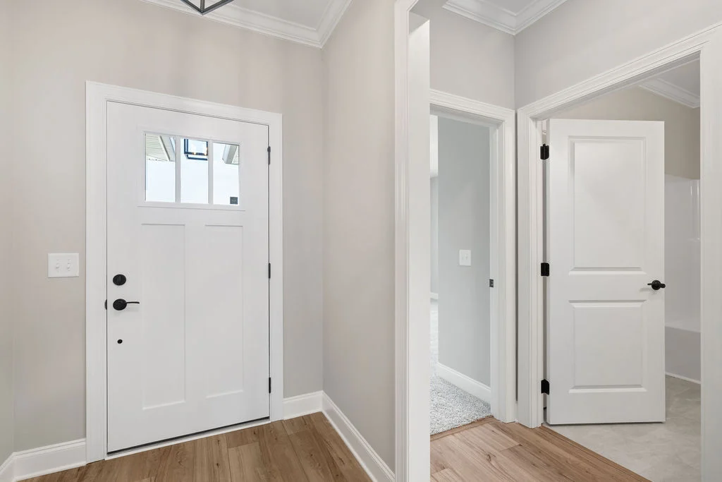White front door with sidelights and wood flooring, leading to interior rooms. Elegant entryway by Pratt Home Builders in Chattanooga TN.