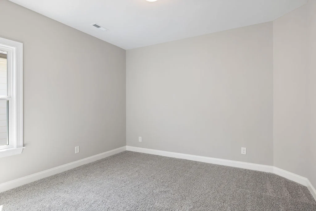 Empty carpeted room with light gray walls and a window, constructed by Pratt Home Builders in Chattanooga TN.