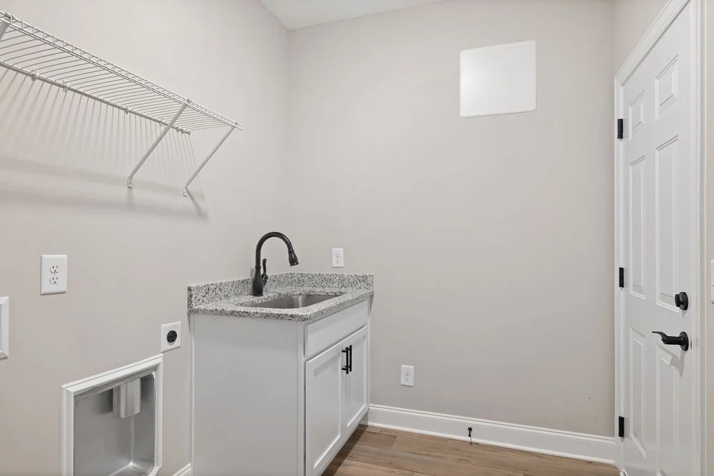 Laundry room with sink, granite countertop, white cabinetry, wall-mounted wire shelf, door, created by Pratt Home Builders in Chattanooga TN.