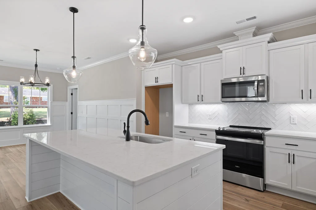 Modern kitchen by Pratt Home Builders in Chattanooga TN, featuring a large island, pendant lights, white cabinets, and herringbone backsplash.