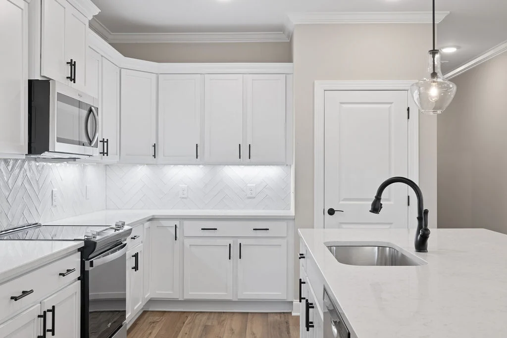Modern kitchen with white cabinets, marble countertops, black fixtures, and wood flooring by Pratt Home Builders in Chattanooga TN.