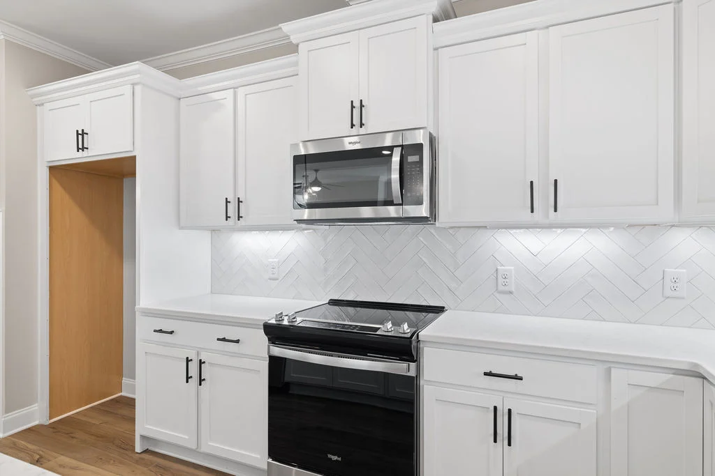 Modern kitchen with white cabinets, stainless steel microwave, and herringbone tile backsplash by Pratt Home Builders in Chattanooga TN.