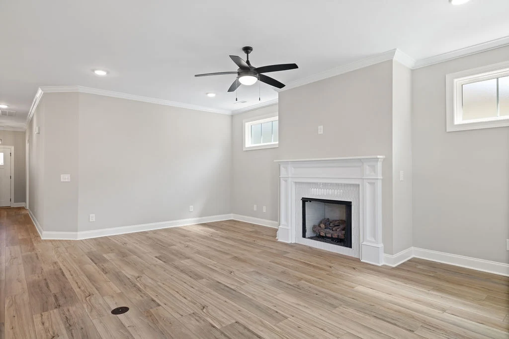 Spacious living room with a white fireplace, wood flooring, ceiling fan, and recessed lighting by Pratt Home Builders in Chattanooga TN.