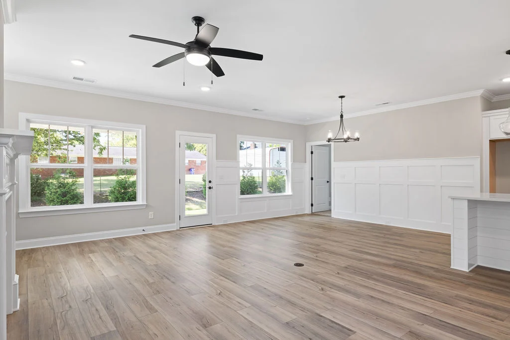 Spacious, well-lit living area with modern fan, chandelier, large windows, and wooden flooring by Pratt Home Builders in Chattanooga, TN.