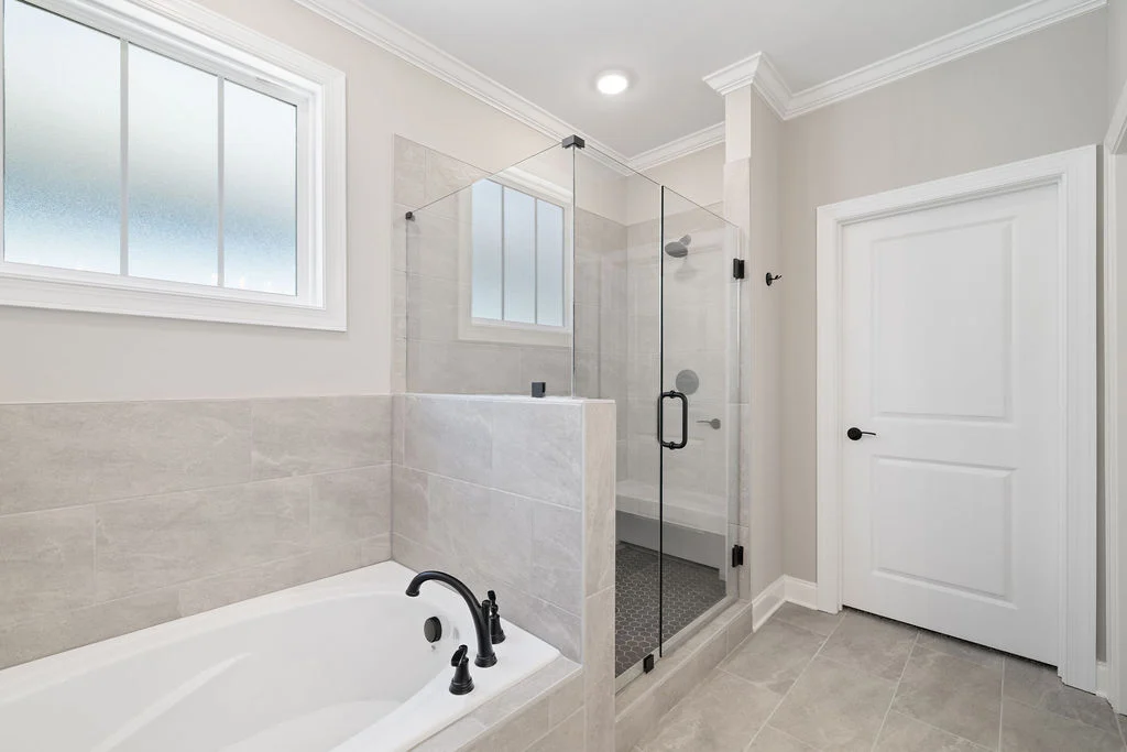 Modern bathroom by Pratt Home Builders in Chattanooga TN, featuring a glass shower, white tub with black fixtures, and large window.