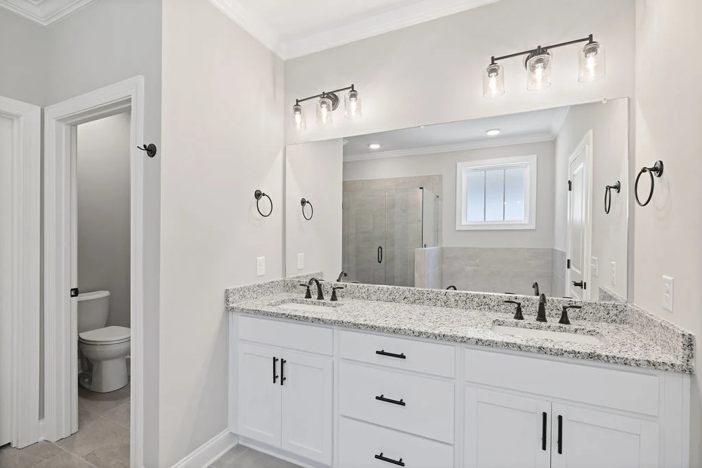 Elegant bathroom by Pratt Home Builders in Chattanooga TN, featuring double vanity with granite countertops, framed mirror, and glass shower enclosure