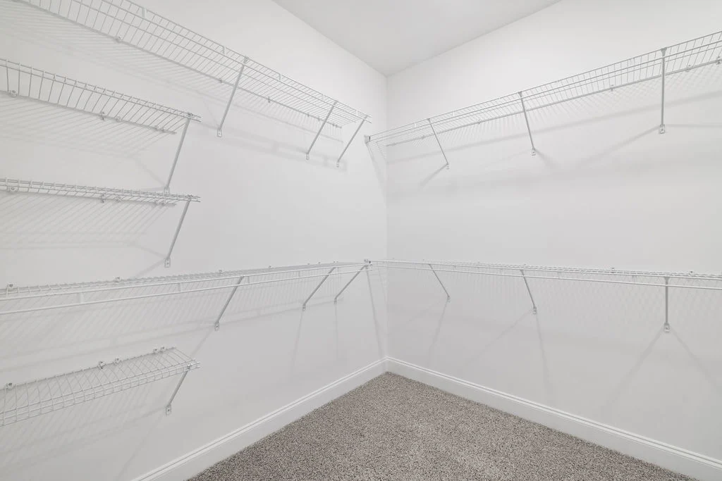 Spacious walk-in closet with white wire shelving on three walls and gray carpeted floor by Pratt Home Builders in Chattanooga, TN.