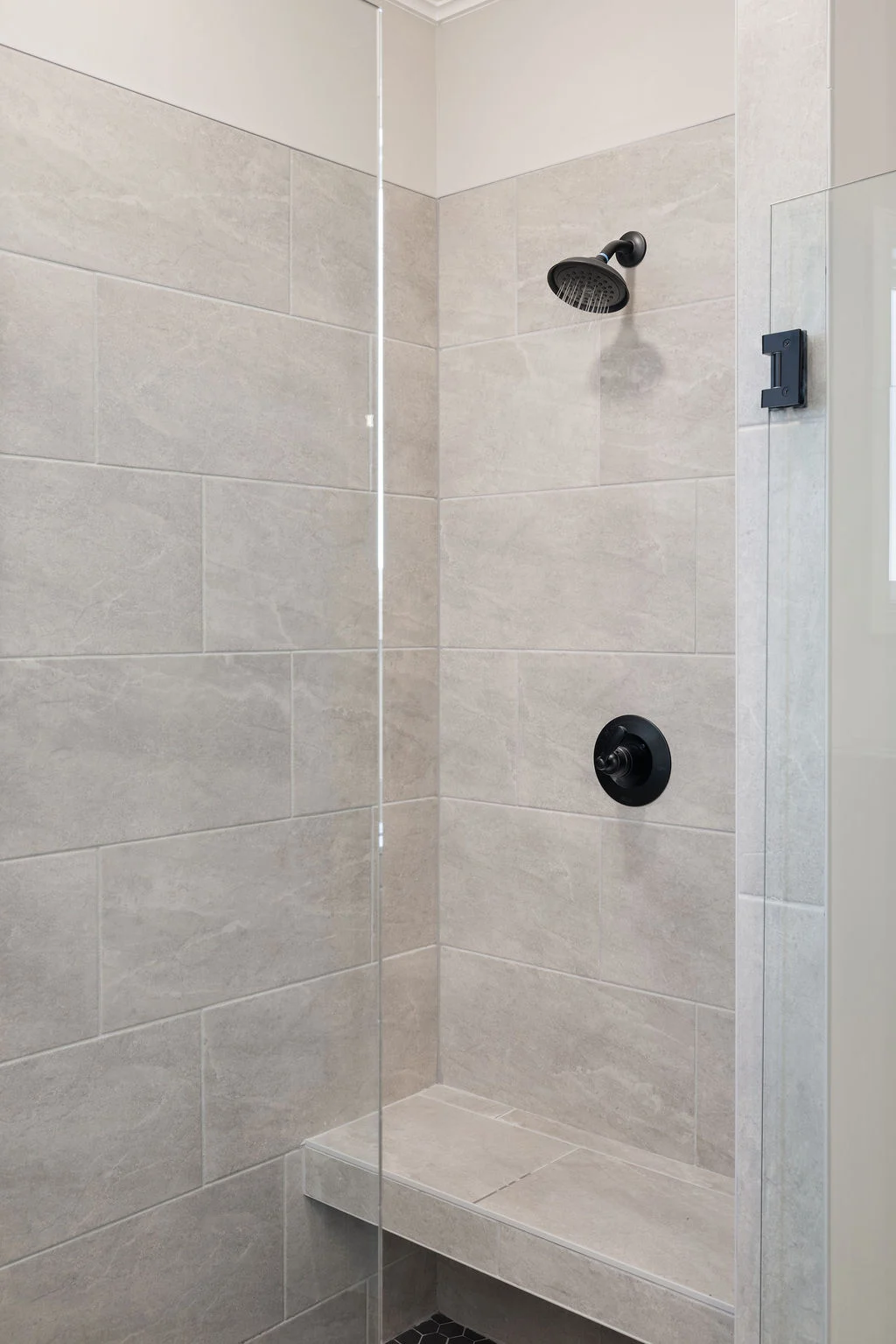 Modern shower with beige tile, black showerhead, and built-in bench by Pratt Home Builders in Chattanooga TN.