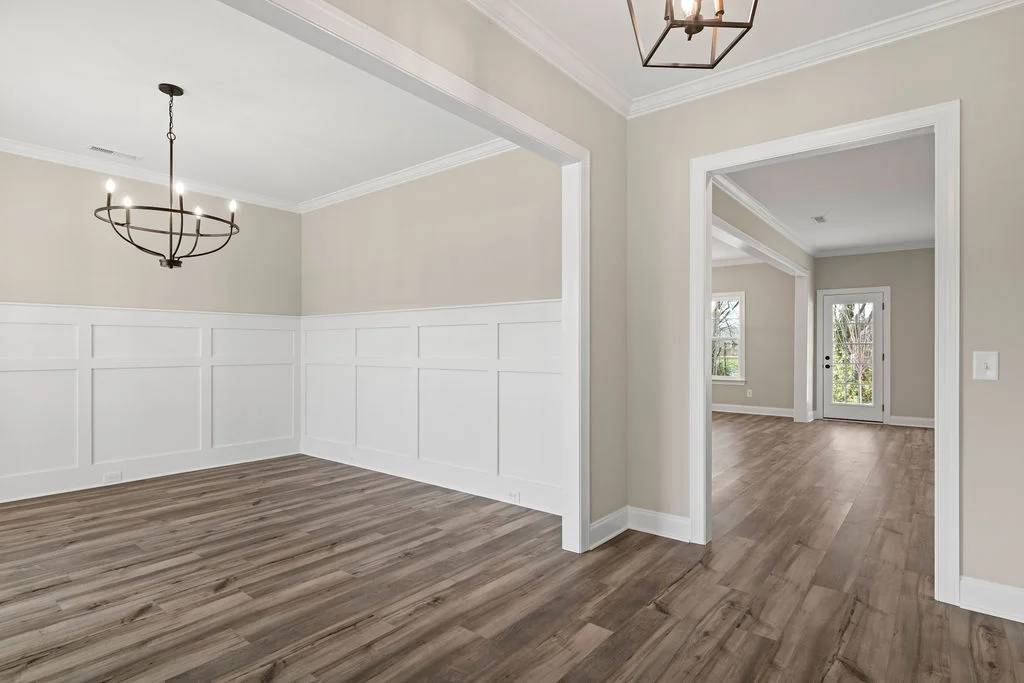 Spacious living area with elegant chandeliers and wood flooring by Pratt Home Builders in Chattanooga TN, featuring white wainscoting and large window