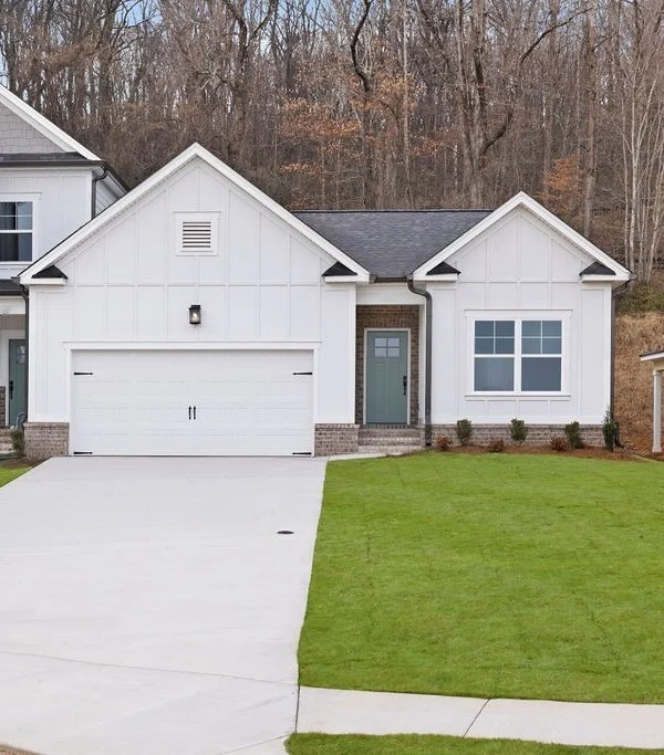 Modern white house with a two-car garage and green lawn, built by Pratt Home Builders in Chattanooga TN, nestled by a leafless forest backdrop.