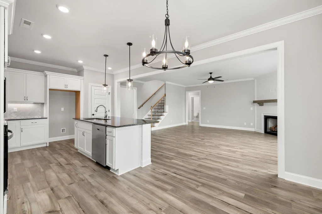 Spacious modern kitchen and living area with hardwood floors, chandelier, and white cabinets by Pratt Home Builders in Chattanooga TN.