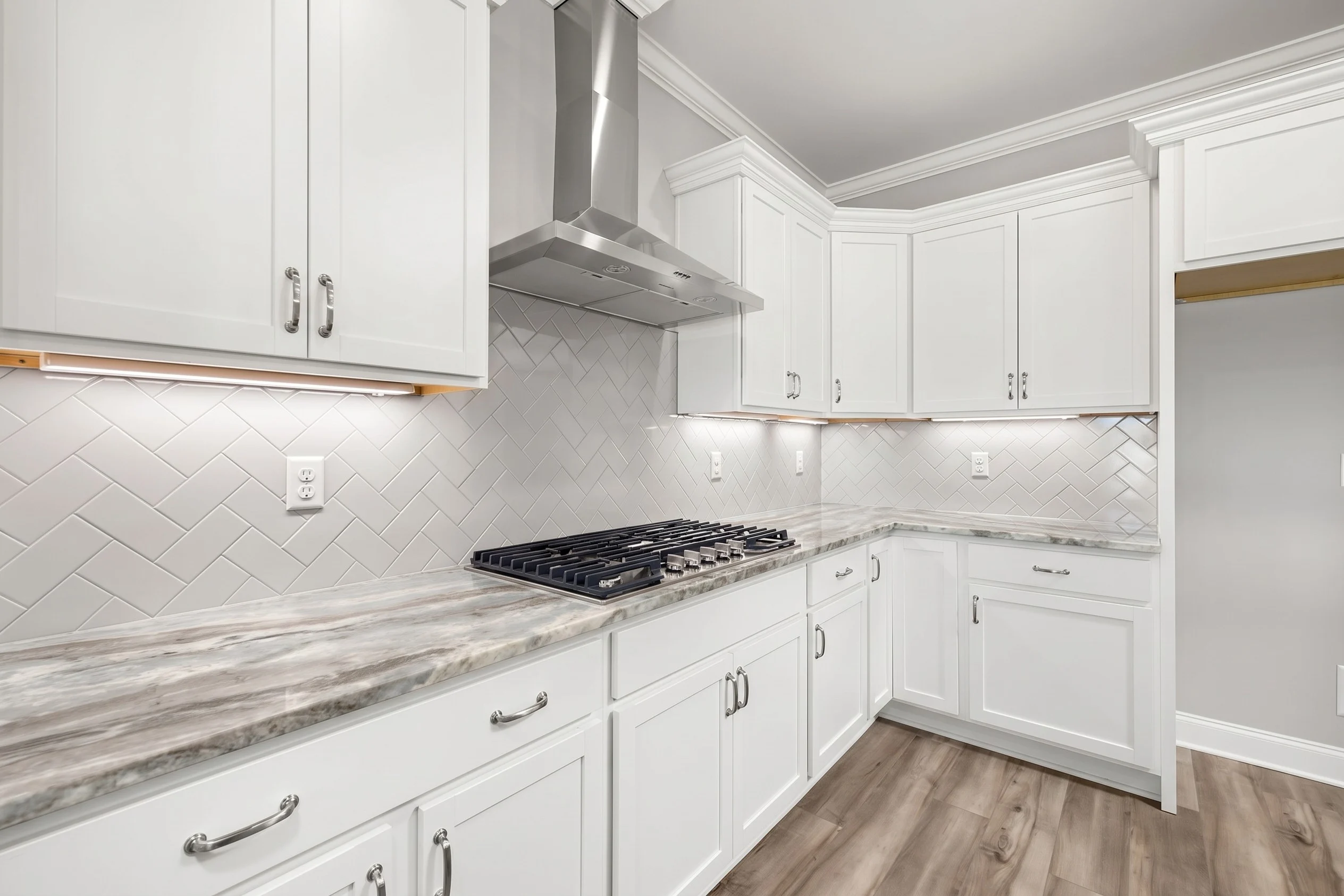 Modern kitchen with white cabinets, herringbone tile backsplash, marble countertop, and stainless stove. Built by Pratt Home Builders in Chattanooga T