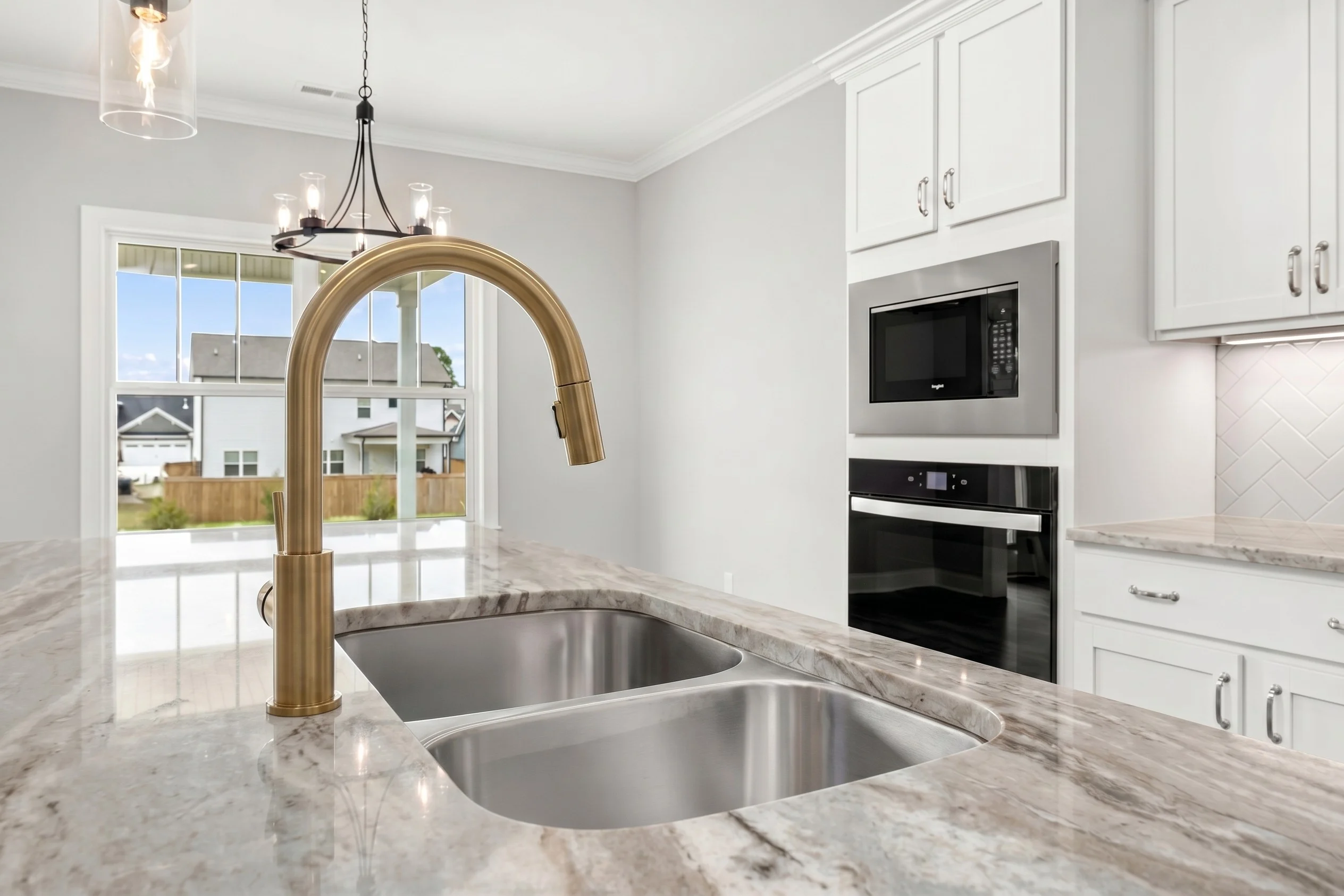 Modern kitchen with marble countertop, brass faucet, double sink, and stainless steel appliances by Pratt Home Builders in Chattanooga TN.