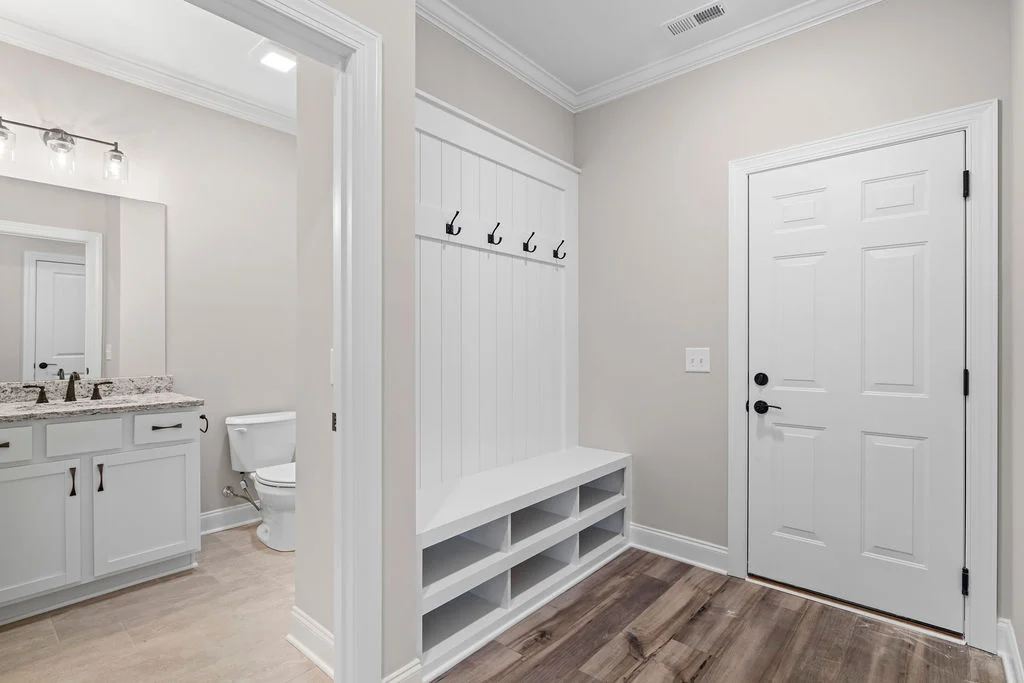 Modern mudroom with storage bench, coat hooks, adjacent bathroom, wood floor, showcasing Pratt Home Builders in Chattanooga TN design.