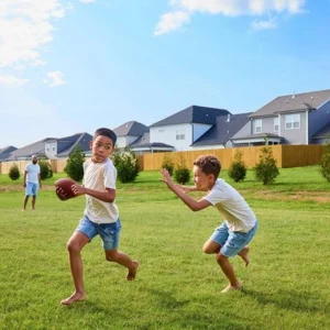 Children playing football on lush green lawn with Pratt Home Builders houses in Chattanooga, TN visible in the background.