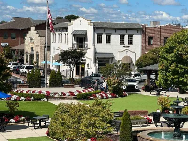 Charming town square with a white building, flag, lush landscaping, and a fountain, associated with Pratt Home Builders in Chattanooga, TN.