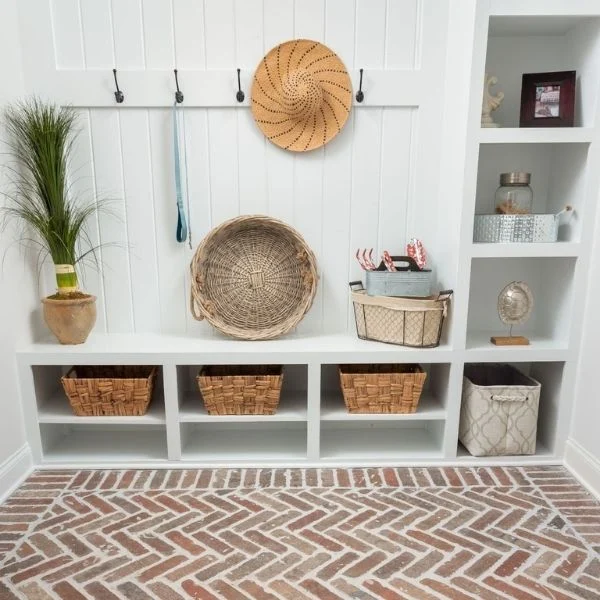 Organized mudroom with baskets, hooks, and decor by Pratt Home Builders in Chattanooga TN, featuring herringbone brick flooring.