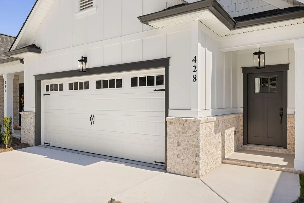 Modern home exterior with white garage doors, brick accents, and a dark front door. Design by Pratt Home Builders in Chattanooga TN.