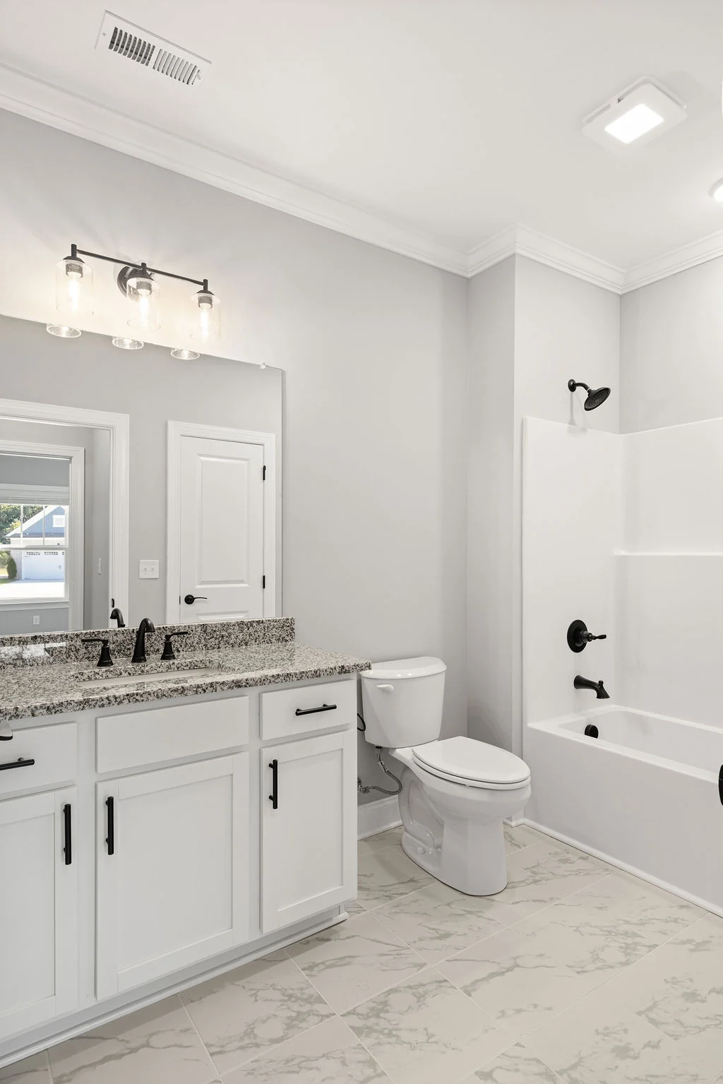 Modern bathroom with white cabinetry, granite countertop, black fixtures, and marble floor tiles by Pratt Home Builders in Chattanooga TN.