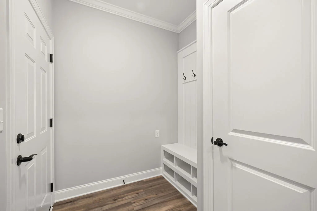 Mudroom with white walls, double doors, wooden floor, hooks, and bench storage. Designed by Pratt Home Builders in Chattanooga TN.