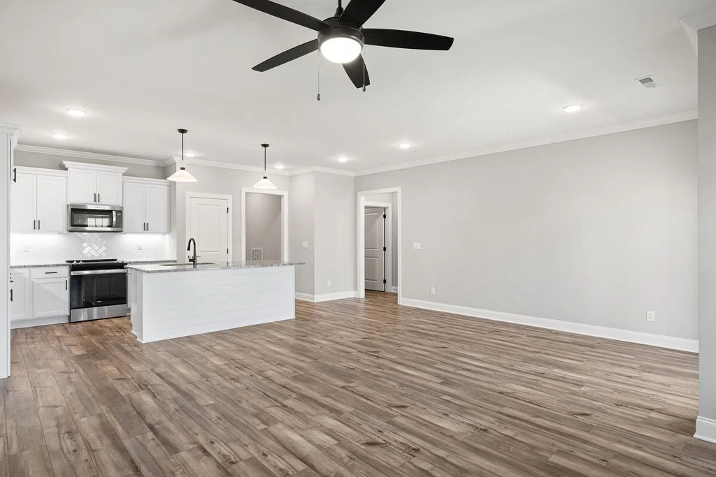 Spacious modern kitchen and living area with hardwood floors, white cabinets, island, and ceiling fan; design by Pratt Home Builders in Chattanooga TN