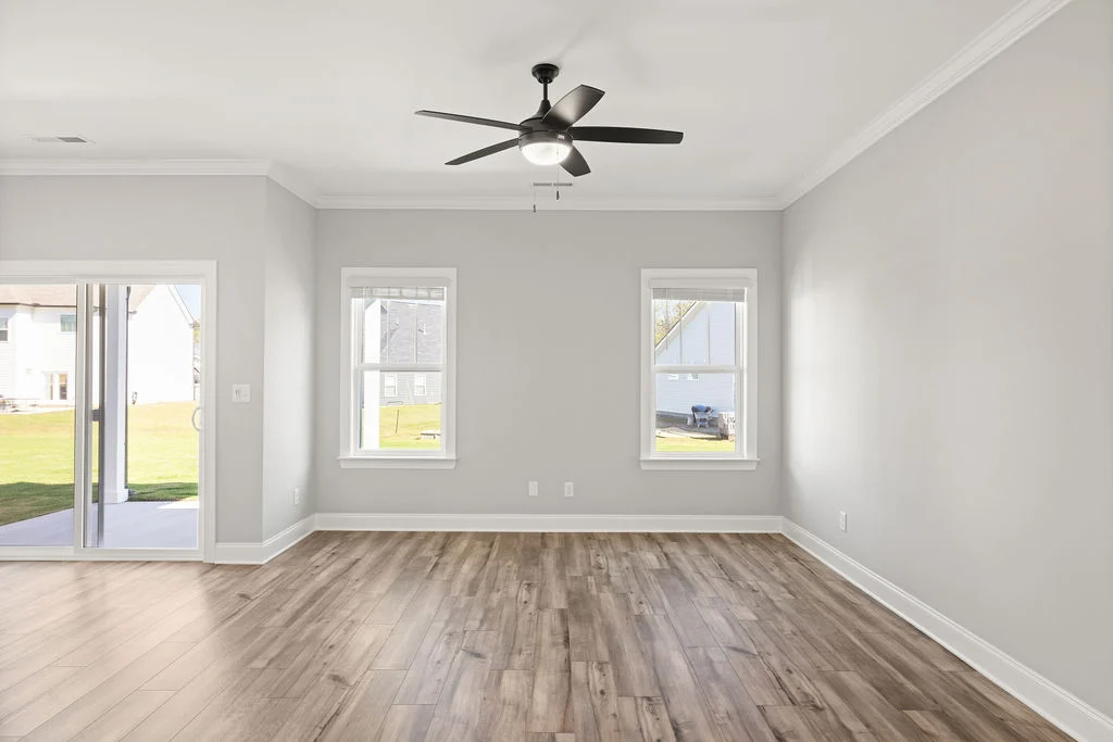 Spacious, empty room with wood flooring, large windows, sliding glass door, and ceiling fan by Pratt Home Builders in Chattanooga TN.
