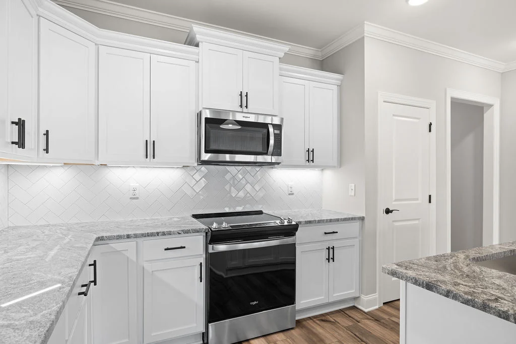 Modern kitchen with white cabinets, herringbone tile backsplash, stainless steel appliances by Pratt Home Builders in Chattanooga TN.