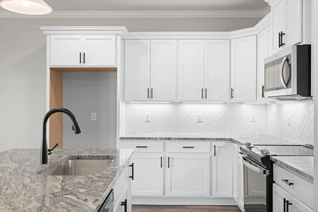 Modern kitchen with white cabinets, granite countertops, black faucet, and stainless appliances. Designed by Pratt Home Builders in Chattanooga, TN.