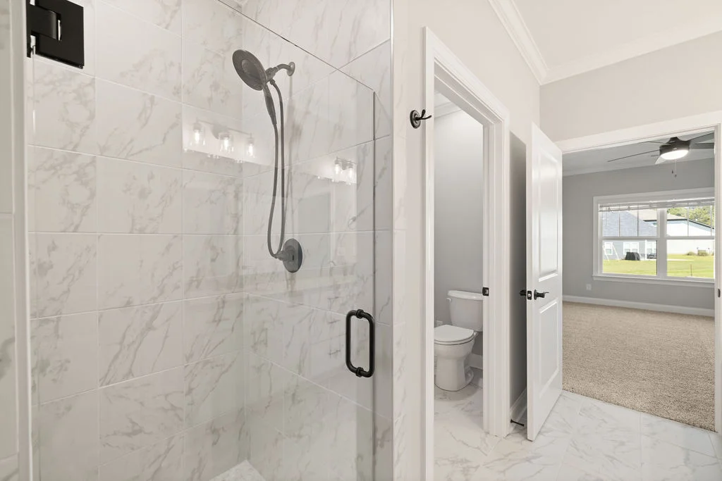 Modern bathroom by Pratt Home Builders in Chattanooga TN, featuring a sleek glass shower, adjacent toilet, and a view into a carpeted room.