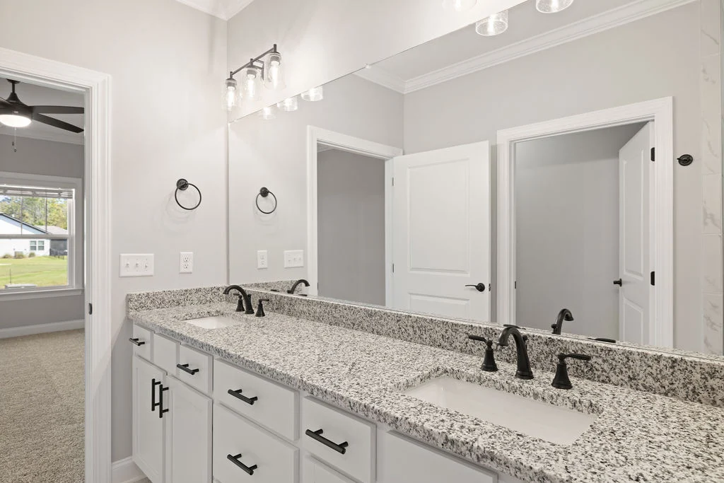 Modern bathroom with granite double vanity, black fixtures, large mirror, and white cabinets by Pratt Home Builders in Chattanooga, TN.