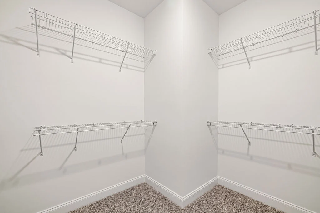 Walk-in closet with white wire shelving by Pratt Home Builders in Chattanooga TN, featuring neutral carpet and pristine white walls.