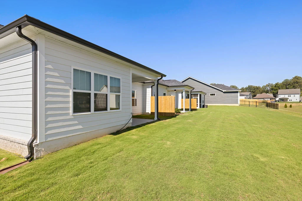 Modern homes with white siding, fenced yards, and manicured lawns under blue sky, built by Pratt Home Builders in Chattanooga TN.