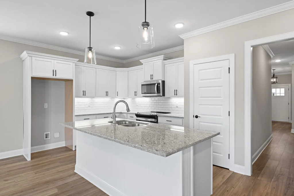Modern kitchen with white cabinets, island, and stainless appliances. Hardwood floors and pendant lighting by Pratt Home Builders in Chattanooga TN.