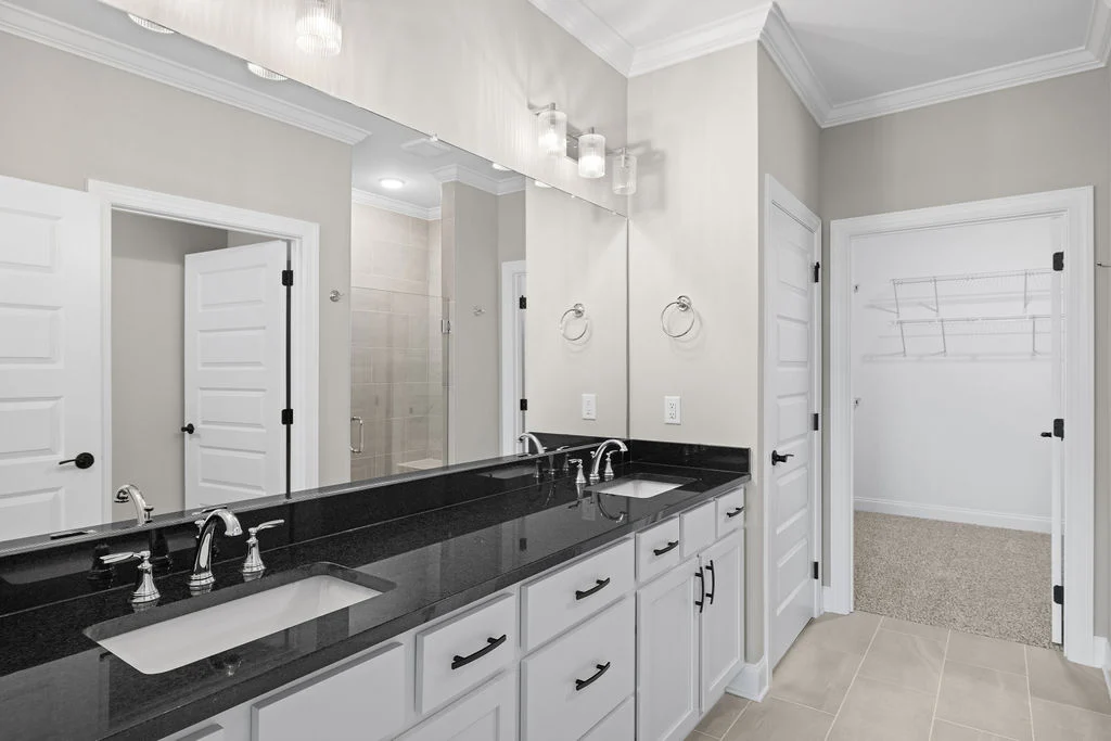 Modern bathroom with double sinks, black granite countertop, large mirror, and white cabinetry by Pratt Home Builders in Chattanooga TN.