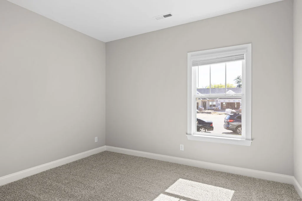 Empty room with beige walls, carpeted floor, and a window view of parked cars and buildings. Built by Pratt Home Builders in Chattanooga TN.