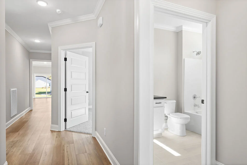 Bright hallway with light wood floors, white doors, and crown molding in a Pratt Home Builders residence, Chattanooga TN. Door open to bathroom.