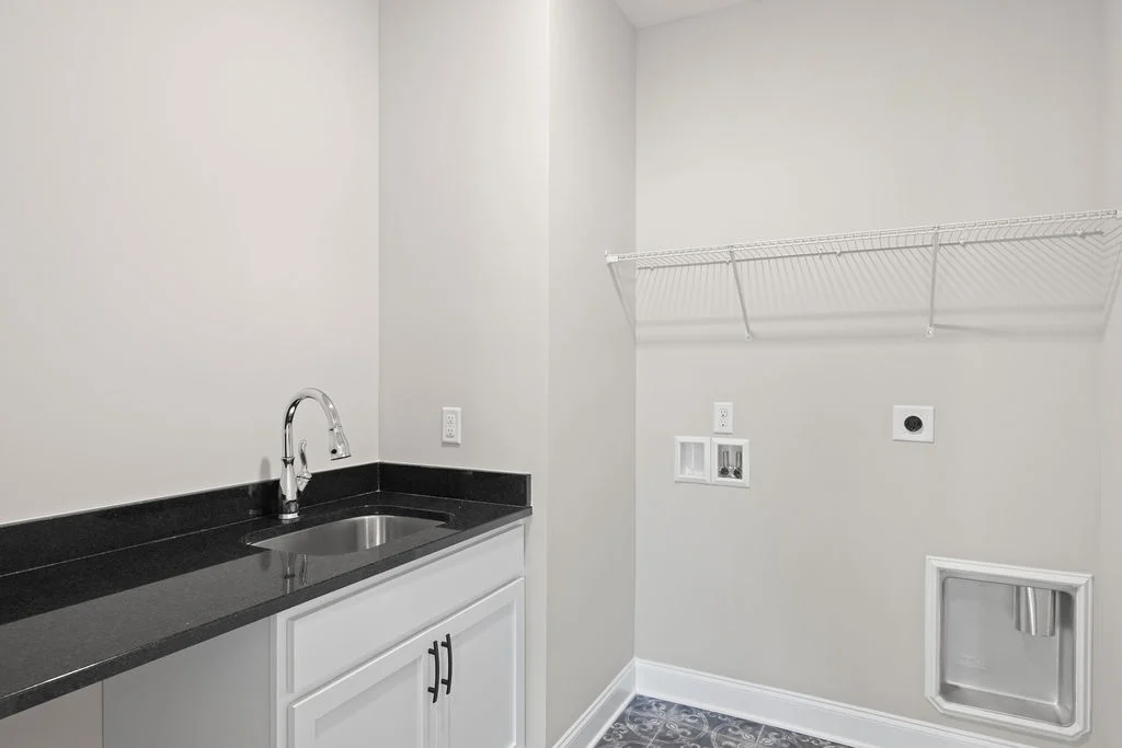 Modern laundry room with a stainless steel sink, dark countertop, and white cabinets by Pratt Home Builders in Chattanooga, TN.