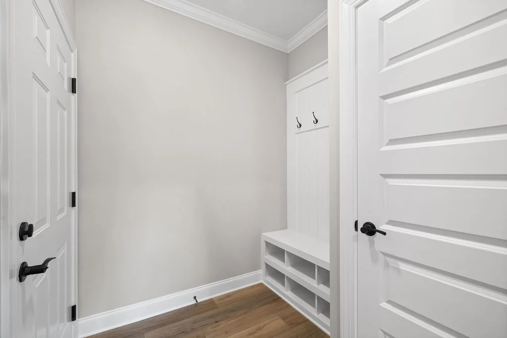 Mudroom by Pratt Home Builders in Chattanooga TN featuring white paneling, bench with storage, and coat hooks between two white doors.